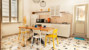 A compact kitchen with a dining area, featuring a wooden table, white and yellow chairs, a microwave, and a coffee maker.