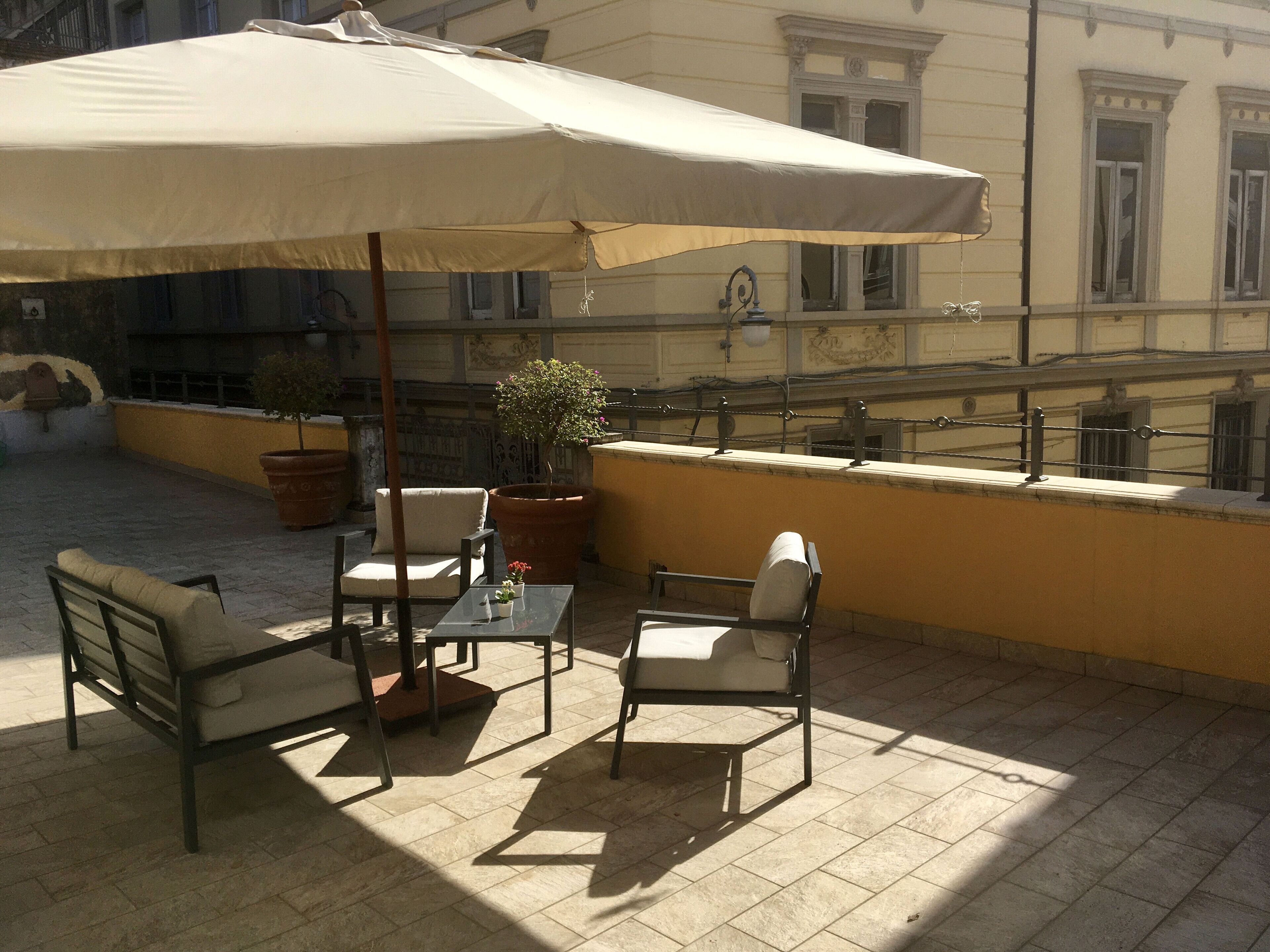 An outdoor seating area with a table and chairs, a large umbrella, and potted plants.