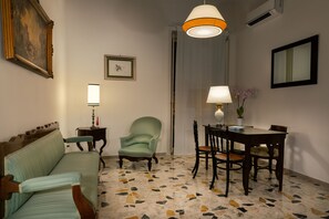 A room with a sofa, a chair, a dining table with chairs, a lamp, a framed picture, and a mirror. - Palazzo Benucci - Residenza di Charme (Santa Maria Capua Vetere)