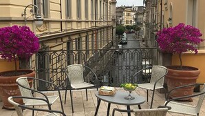 An outdoor terrace with wicker chairs and a table, surrounded by potted plants and a view of a narrow street. - Palazzo Benucci - Residenza di Charme (Santa Maria Capua Vetere)