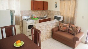 Cocina compacta con estufa, microondas y pileta. Hay una mesa de comedor con sillas y un sofá con almohadones.