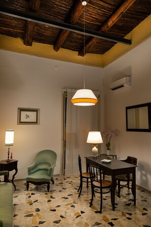 A dining area with a wooden ceiling, a table with chairs, a green armchair, and a patterned floor. - Palazzo Benucci - Residenza di Charme (Santa Maria Capua Vetere)