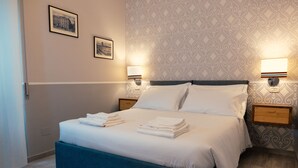 A neatly made bed with folded towels, two wall-mounted lamps, and framed pictures on the wall. - Palazzo Benucci - Residenza di Charme (Santa Maria Capua Vetere)