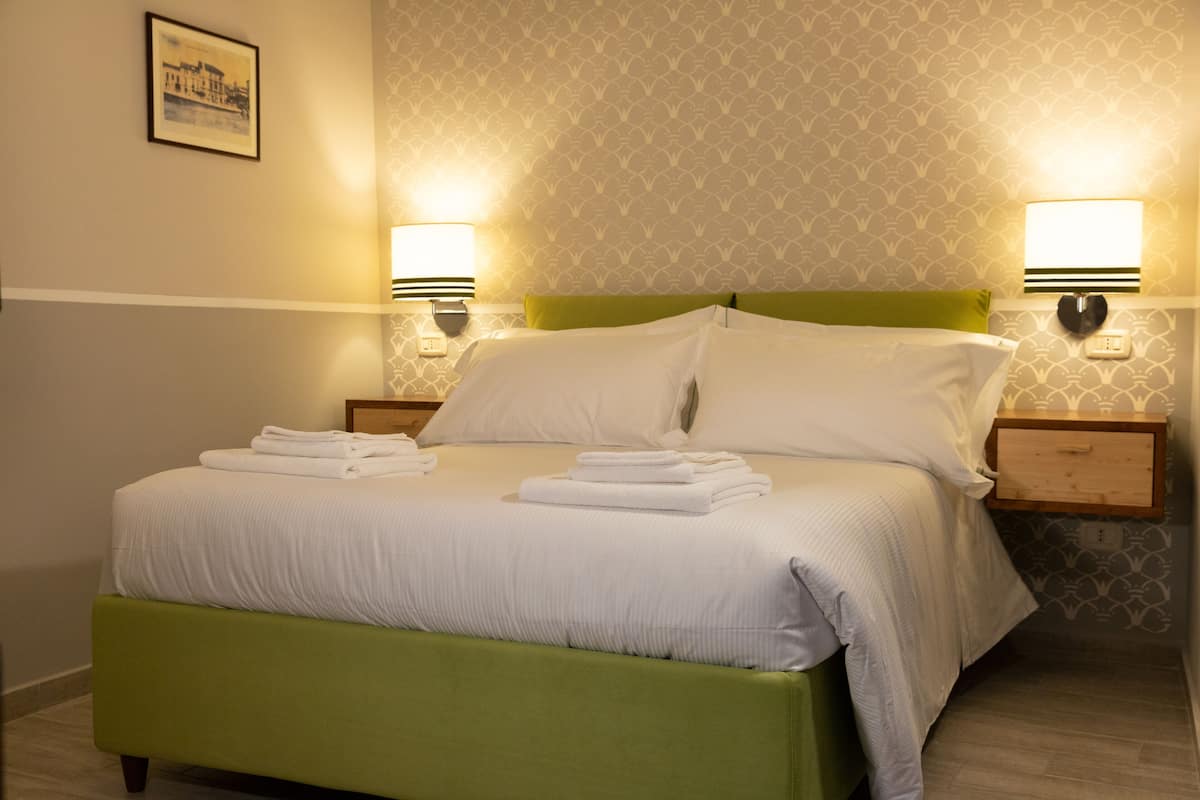 A neatly made bed with white linens and pillows, two bedside lamps, and a green headboard.
