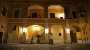 A courtyard with a staircase leading to an upper level, surrounded by arches and potted plants. - Palazzo Benucci - Residenza di Charme (Santa Maria Capua Vetere)