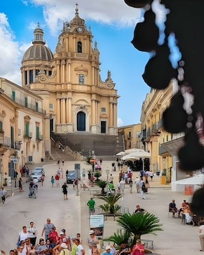 A historic building with a dome and bell tower, surrounded by a plaza with people and outdoor seating. - Eco-friendly Holiday Apartment Marina di Ragusa apt "il Gufo" (Ragusa)