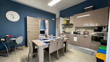 A modern kitchen with stainless steel appliances, a dining area with a wooden table and chairs, and a blue accent wall with a clock.