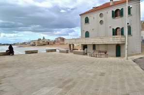 Um edifício à beira-mar com varanda, um banco e vista para o mar.
