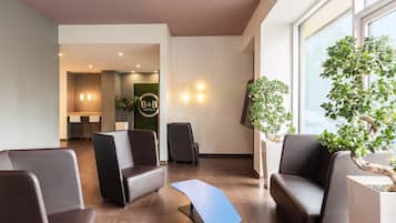 A modern hotel lobby with seating areas, a reception desk, and a large window providing natural light.