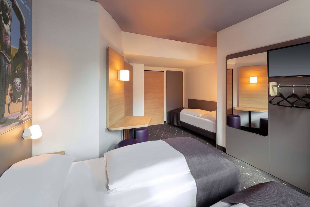 A hotel room with two beds, a small table, a mirror, and a wall-mounted light fixture.
