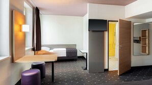 A modern hotel room with a bed, a desk, a chair, a small table, and a mirror. - B&B Hotel Düsseldorf-Mitte (Düsseldorf)