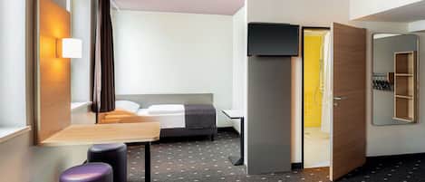A modern hotel room with a bed, a desk, a chair, a small table, and a mirror.