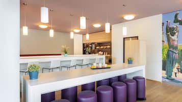 A modern bar area with white bar stools, purple barstools, pendant lighting, and a counter with a plant.