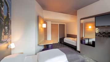 A hotel room with two beds, a small table, a mirror, and a wall-mounted light fixture.