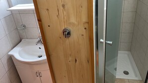 Une salle de bain avec une porte en bois, un lavabo blanc et une cabine de douche en verre.