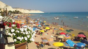 Une plage où l’on voit des gens nager et bronzer, des parasols et un bâtiment agrémenté de fleurs.