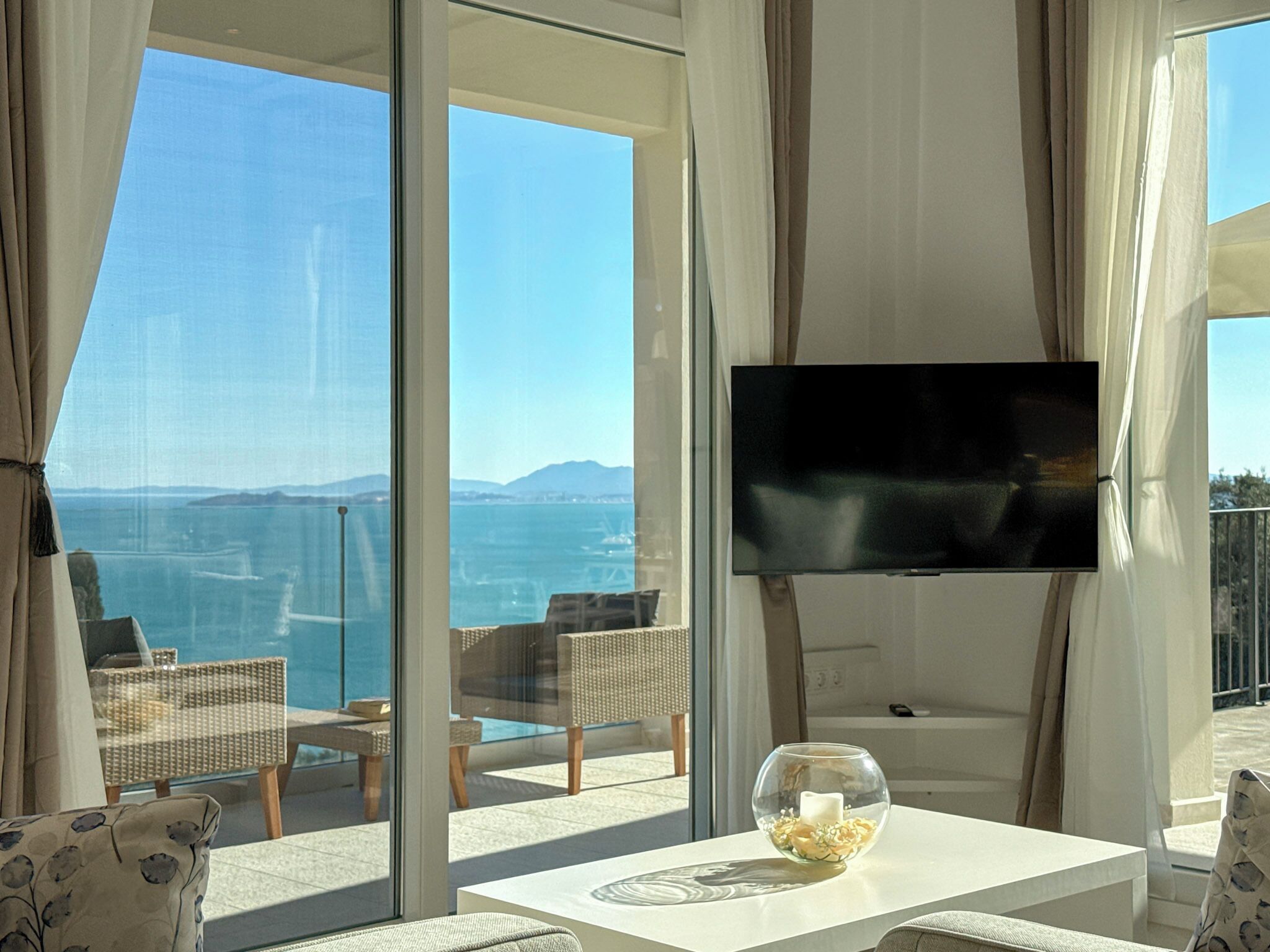 A modern room with a large TV, comfortable seating, and a view of the sea.