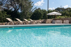 Ein Swimmingpool mit klarem, blauem Wasser, umgeben von Liegestühlen und einer Steinmauer.