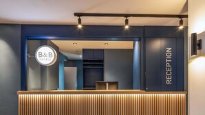 Een receptiebalie met een B&B Hotels bord, een receptiegedeelte en een keuken die door het glas zichtbaar is.