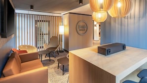 Een hotel receptie met een houten balie, twee stoelen, een bank, een tv aan de muur en een bordje met de tekst 'B&B HOTELS'.