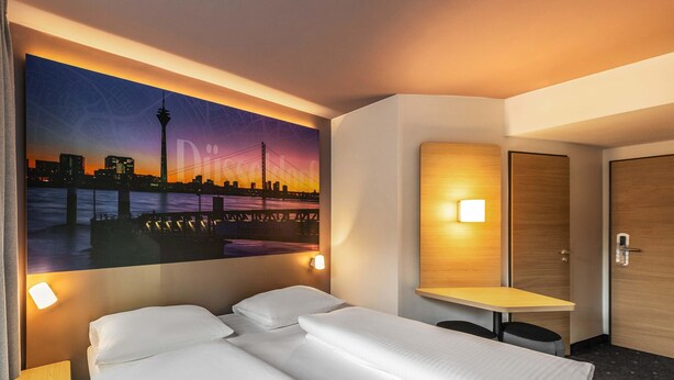 Een hotelkamer met een bed, een bureau, een muurlamp en een schilderij van een stadsgezicht.