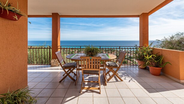 Een balkon met een tafel en stoelen, plantenbakken en uitzicht op zee.
