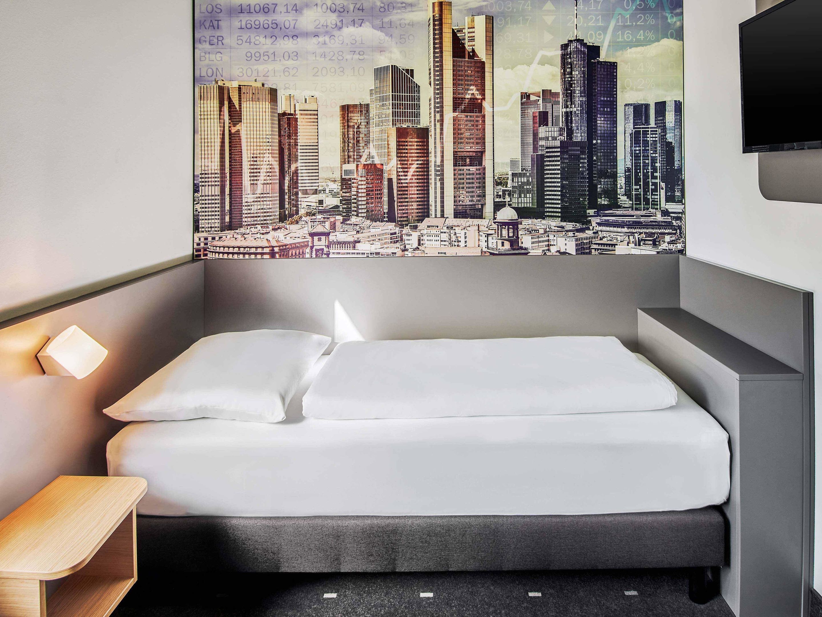A hotel room with a bed, a nightstand, and a cityscape mural on the wall.