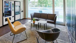 A modern lounge area with a sofa, a lounge chair, a small table with a plant, and vending machines. - B&B Hotel Frankfurt-West (Frankfurt)