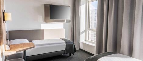 Una habitación de hotel con cama, escritorio, televisión y ventana con cortinas.