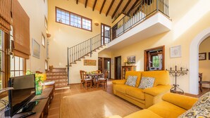 Un vaste espace de vie avec un plafond haut, un escalier, un canapé jaune et une table à manger.