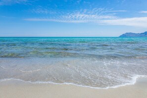 A beach with clear water, a sandy shore, and distant mountains.