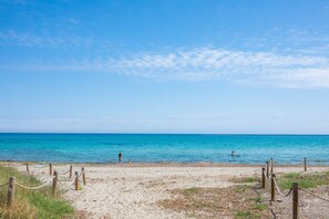 Una playa con cielo despejado, orilla arenosa y algunas personas a lo lejos.