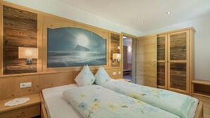Un dormitorio con una cama, dos mesitas de noche, una lámpara auxiliar, un cuadro en la pared y armarios de madera.
