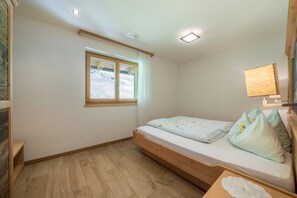 Una camera piccola con un letto singolo, pavimento in legno, una finestra vista, un comodino e una lampada a parete.