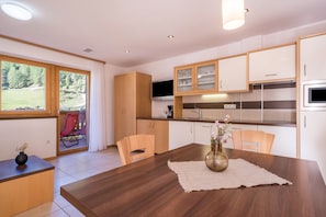 Une cuisine moderne avec des meubles en bois, une table à manger avec des chaises, et une vue sur un paysage verdoyant grâce à de grandes fenêtres.