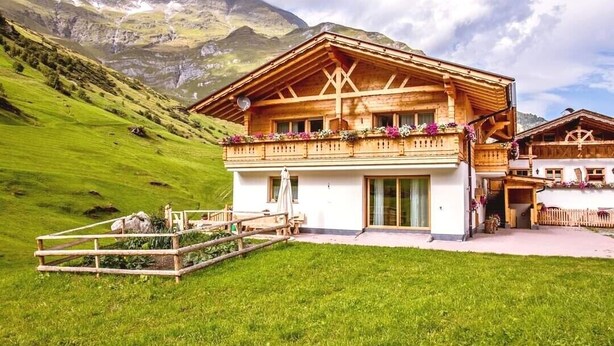 Un bâtiment de style chalet doté d’un balcon, entouré de collines et de montagnes verdoyantes.
