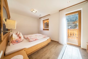Une chambre à coucher avec un lit en bois, une fenêtre donnant sur un immeuble et un luminaire au plafond.