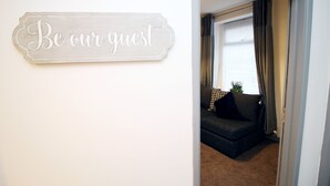 A sign that reads "Be our guest" in a room with a dark-colored sofa and a window with curtains. - BOOM Swansea City (Swansea)