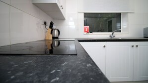 A kitchen with white cabinets, a black countertop, a stove, a sink, and a window above the sink. - BOOM Swansea City (Swansea)