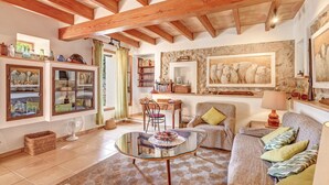 A cozy living room with a glass coffee table, a sofa, a bookshelf, and a stone wall with artwork. - "Ca les Estamenyes" near the sea, Wi-Fi, air conditioning, garden and pool (POLLENÇA)
