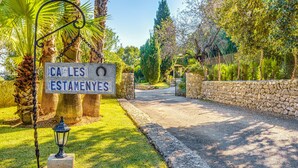 A stone pathway leading to a gated entrance, surrounded by lush greenery and palm trees. - "Ca les Estamenyes" near the sea, Wi-Fi, air conditioning, garden and pool (POLLENÇA)