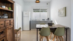 Une cuisine compacte équipée d’un réfrigérateur, d’un évier et de meubles de rangement en bois. On y trouve une table à manger avec des chaises et un luminaire suspendu.
