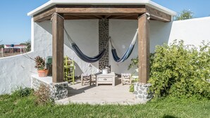 Un espace extérieur abrité, avec une table et des chaises, un hamac et une plante en pot.