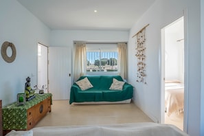 A room with a green sofa, a wooden cabinet, a statue, a wall hanging, and a window with curtains.