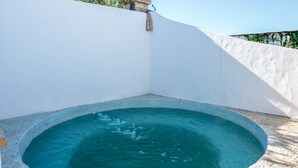 Une petite piscine ronde à l’eau d’un bleu limpide, entourée d’un mur blanc et dont le sol est recouvert de petits galets.