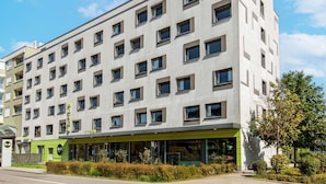 A multi-story hotel with a modern design, featuring a green reception area and multiple windows.