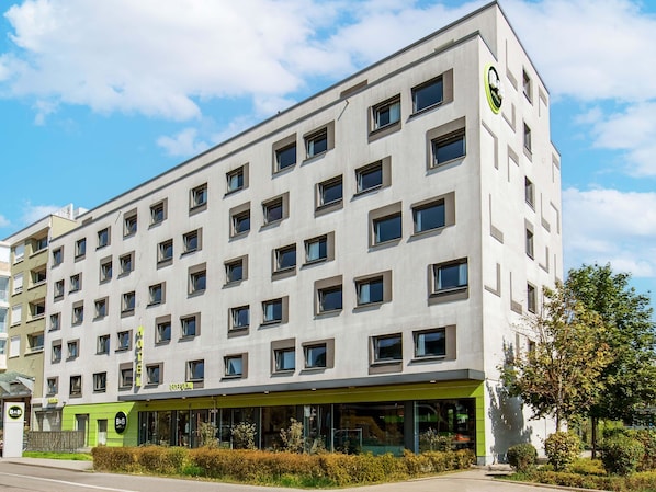 Un hotel de varios pisos con un diseño moderno, que cuenta con una recepción verde y numerosas ventanas.