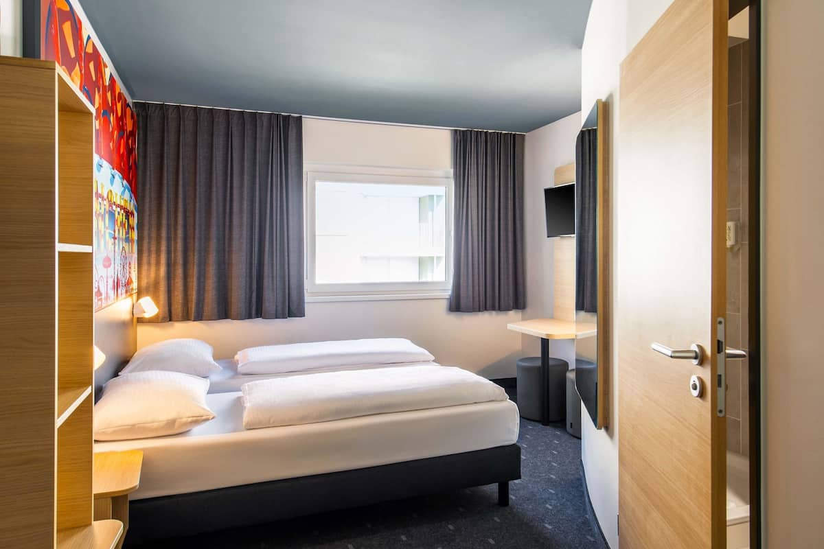 A hotel room with a bed, a desk, a TV, and a window with curtains.