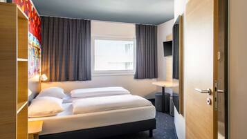 A hotel room with a bed, a desk, a TV, and a window with curtains.