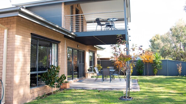 A modern house with a covered patio, a brick exterior, and a fenced yard.
